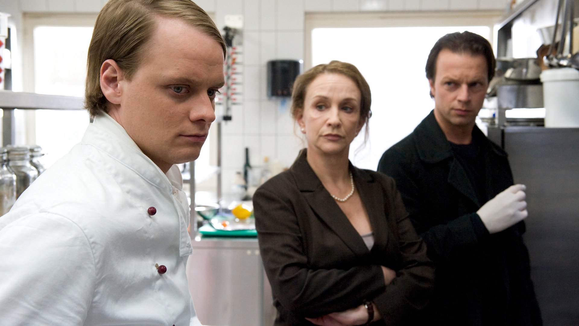 "SOKO Wismar - Tiefe Wunden": Moni Falkner (Cornelia Lippert) und Sven Herzog (Michael Härtle) stehen in einer großen Restaurant-Küche dem Koch Mark Schmidt (Stefan Konarske) gegenüber. Michael Härle trägt weiße Gummihandschuhe und Moni Falkner hat die Arme vor der Brust verschränkt.