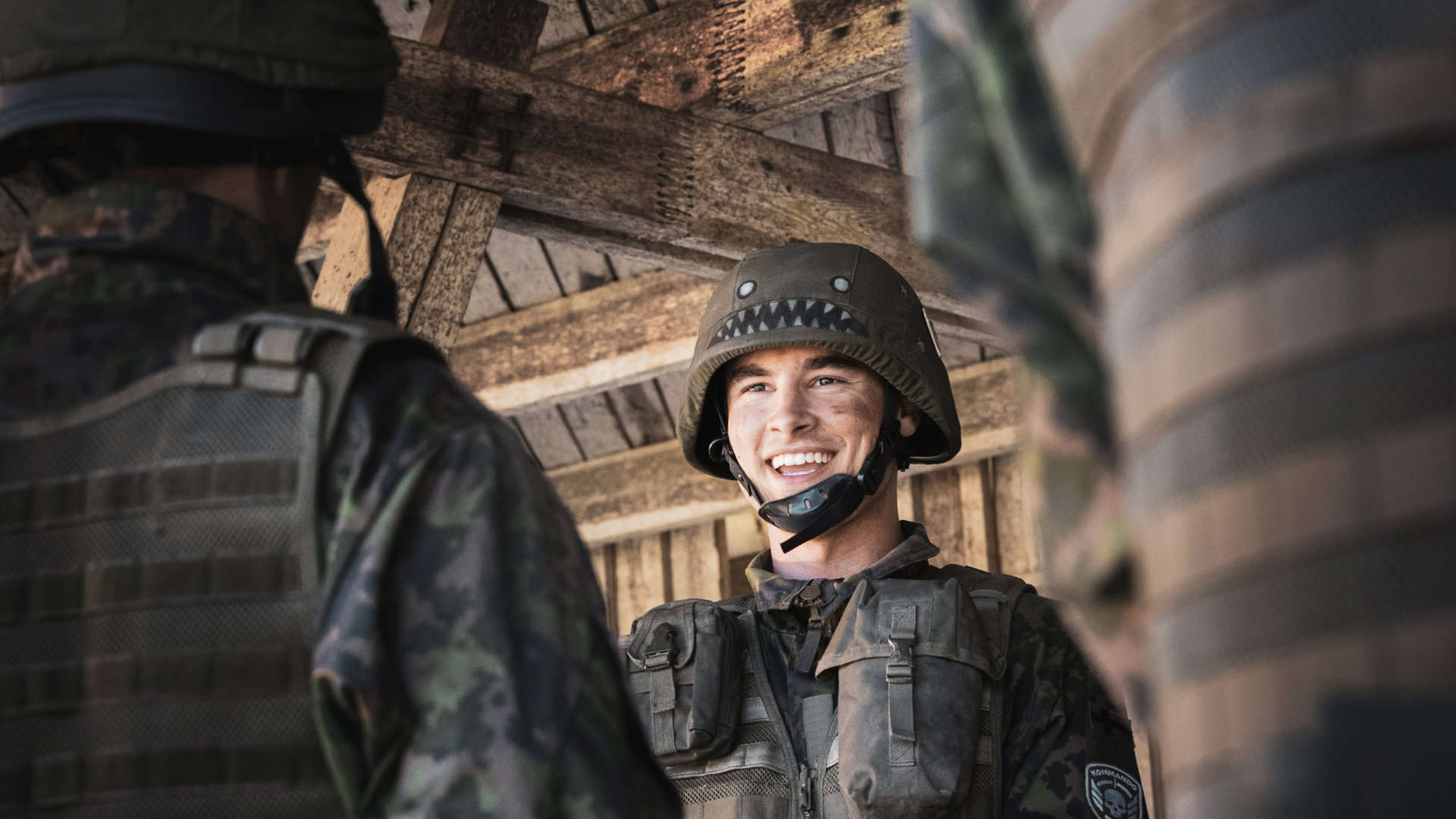 "Californian Commando - Fünf Schüsse aufs Ziel": Van (Kian Lawley) steht in militärischer Kampfausrüstung inmitten mehrerer Soldaten und schaut lächelnd zur Seite.