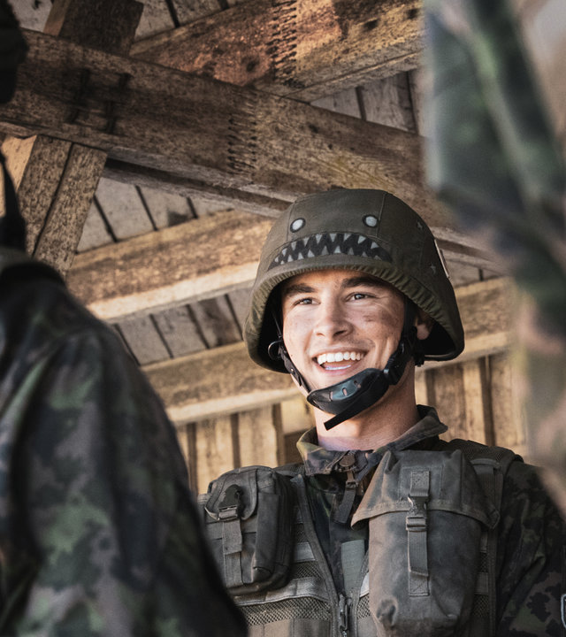 "Californian Commando - Fünf Schüsse aufs Ziel": Van (Kian Lawley) steht in militärischer Kampfausrüstung inmitten mehrerer Soldaten und schaut lächelnd zur Seite.
