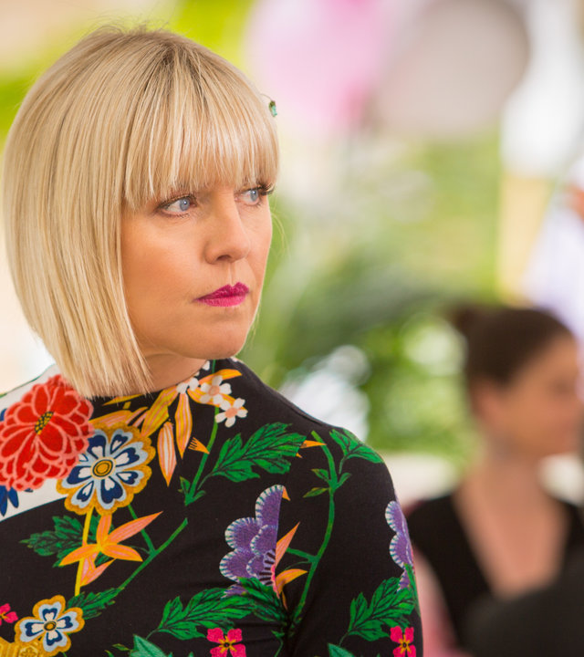 "Agatha Raisin – Und der tote Auftragskiller Teil 1": Agatha Raisin (Ashley Jensen) schaut sich aufmerksam im Festzelt um, während sie ein Glas Sekt in der Hand hält.