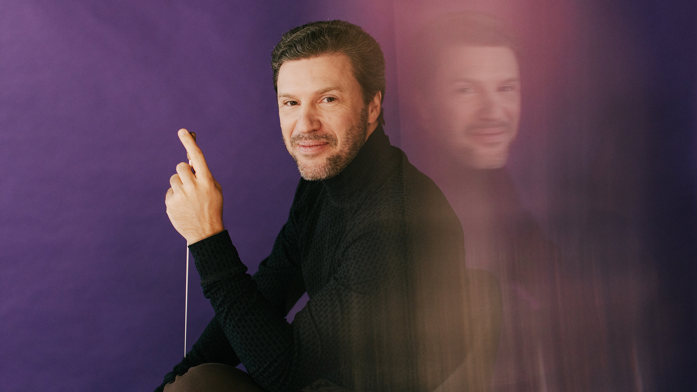 "Hannover Klassik Open Air 2025 – Die große Opern-Gala": Chefdirigent Stanislav Kochanovsky sitzt in die Kamera blickend mit Taktstock vor lila Hintergrund.