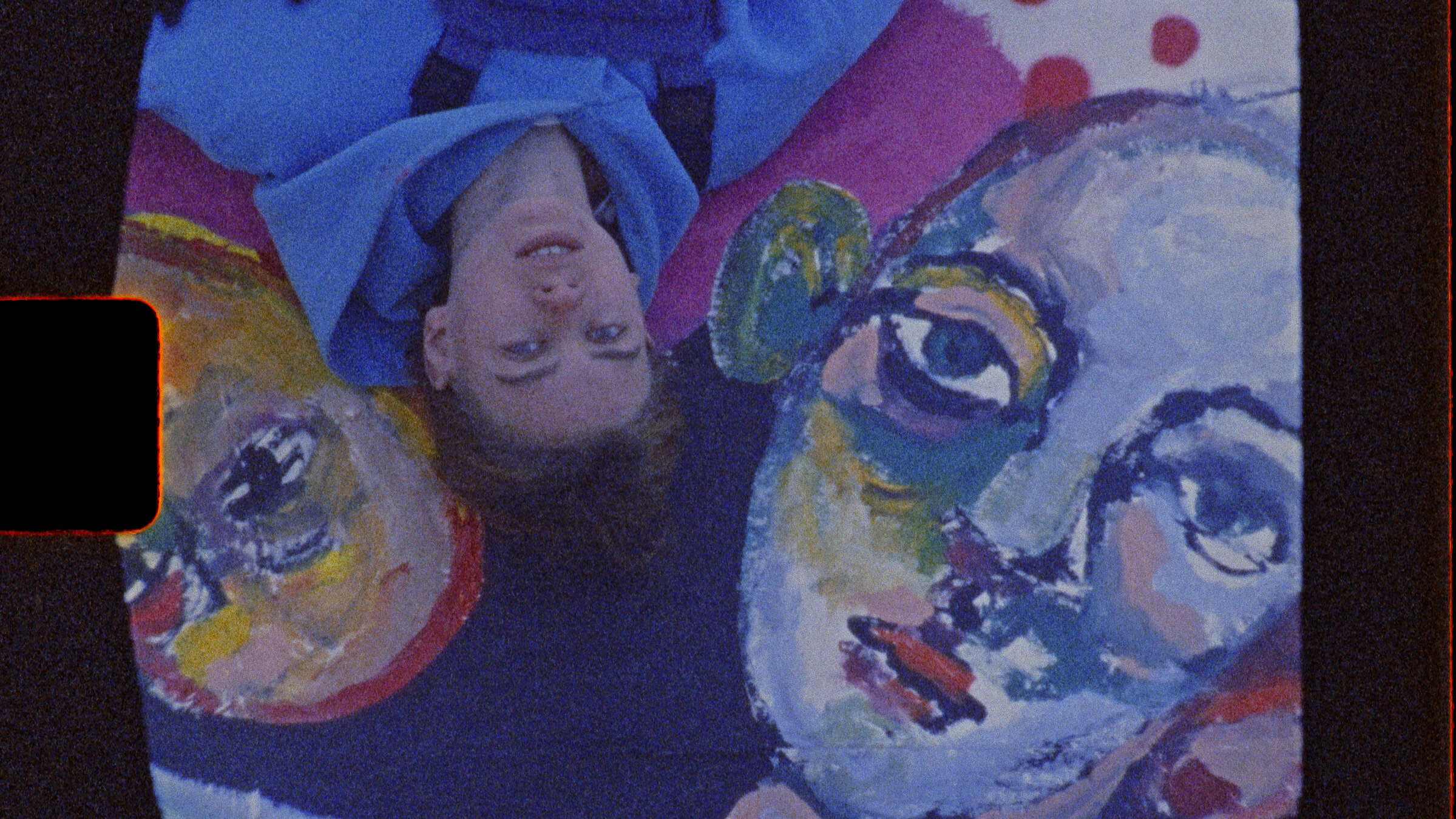 "DocuMe - Alice in Paris": Junge Frau von oben fotografiert liegt neben farbigen Kunstporträts.