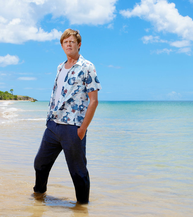 "Death in Paradise - Die einsame Insel": Humphrey (Kris Marshall) steht mit den Füßen im Wasser am Strand und blickt Richtung Kamera.