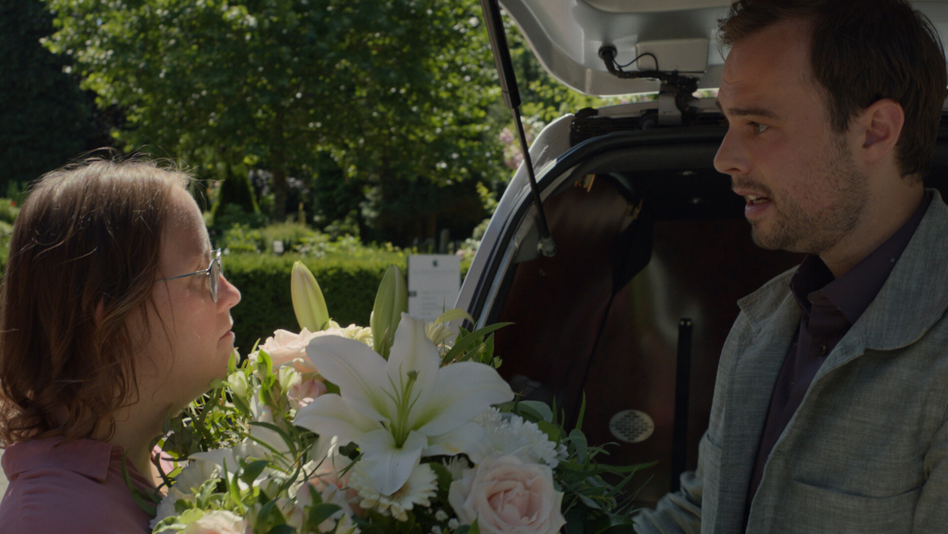 "Notruf Hafenkante - Lila und der Tod": Lila (Carina Kühne) und Oskar (Tom Gronau) stehen sich hinter einer geöffneten Kofferraumklappe eines Pkw gegenüber. Oskar gibt Lila ein Blumengesteck.