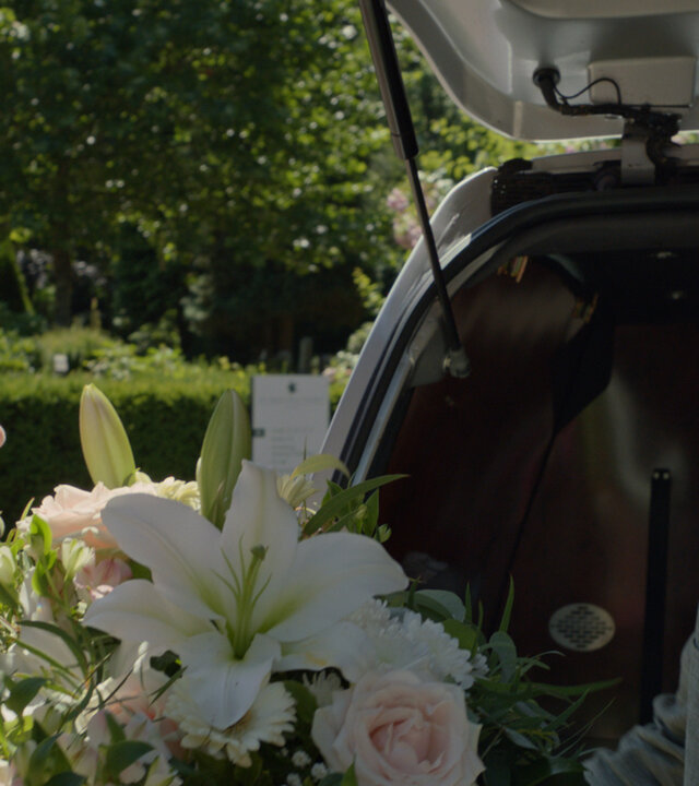 "Notruf Hafenkante - Lila und der Tod": Lila (Carina Kühne) und Oskar (Tom Gronau) stehen sich hinter einer geöffneten Kofferraumklappe eines Pkw gegenüber. Oskar gibt Lila ein Blumengesteck.