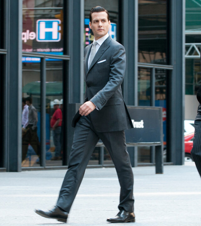 "Suits - Schmutzige kleine Geheimnisse": Harvey (Gabriel Macht) und Mike (Patrick J. Adams) gehen nebeneinander an einer gläsernen Häuserfront entlang. Beide tragen dunkle Anzüge, Mike hat die Hände in den Hosentaschen, Harvey blickt entschlossen zur Seite.