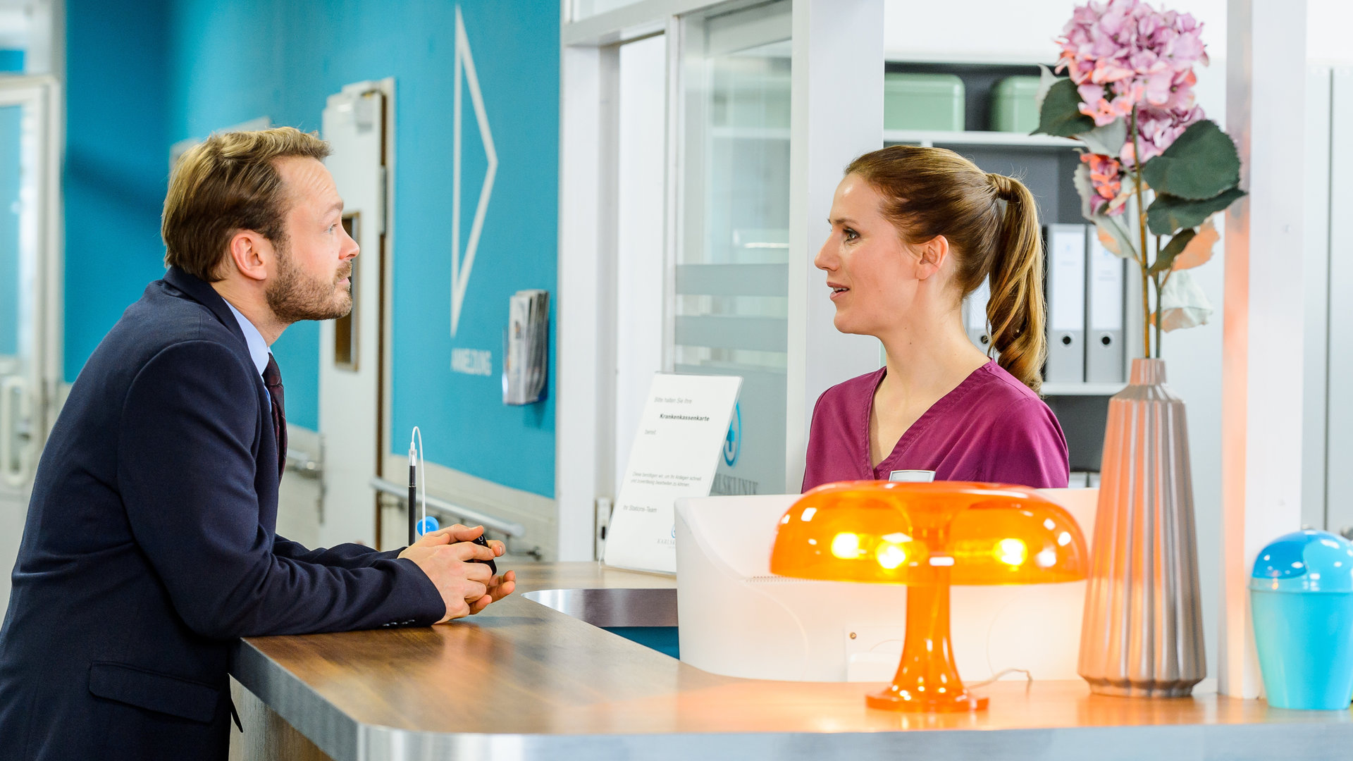 "Bettys Diagnose - Unter Druck": Jan Petersen hat beide Arme auf dem Tresen der Schwesterkanzel abgestützt und unterhält sich mit Betty (Bettina Lamprecht).
