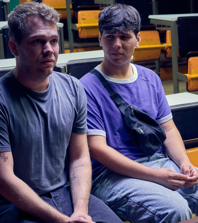 "Like a Loser - Bitterer Ernst": Julian (Ben Münchow) und Ernst (Diyar Ilhan) sitzen auf zwei Stühlen der vordersten Schulbank. Julian blickt nach vorne in Richtung Pult, Ernst sieht ihn an. Beide halten ihre Arme eng am eigenen Körper.