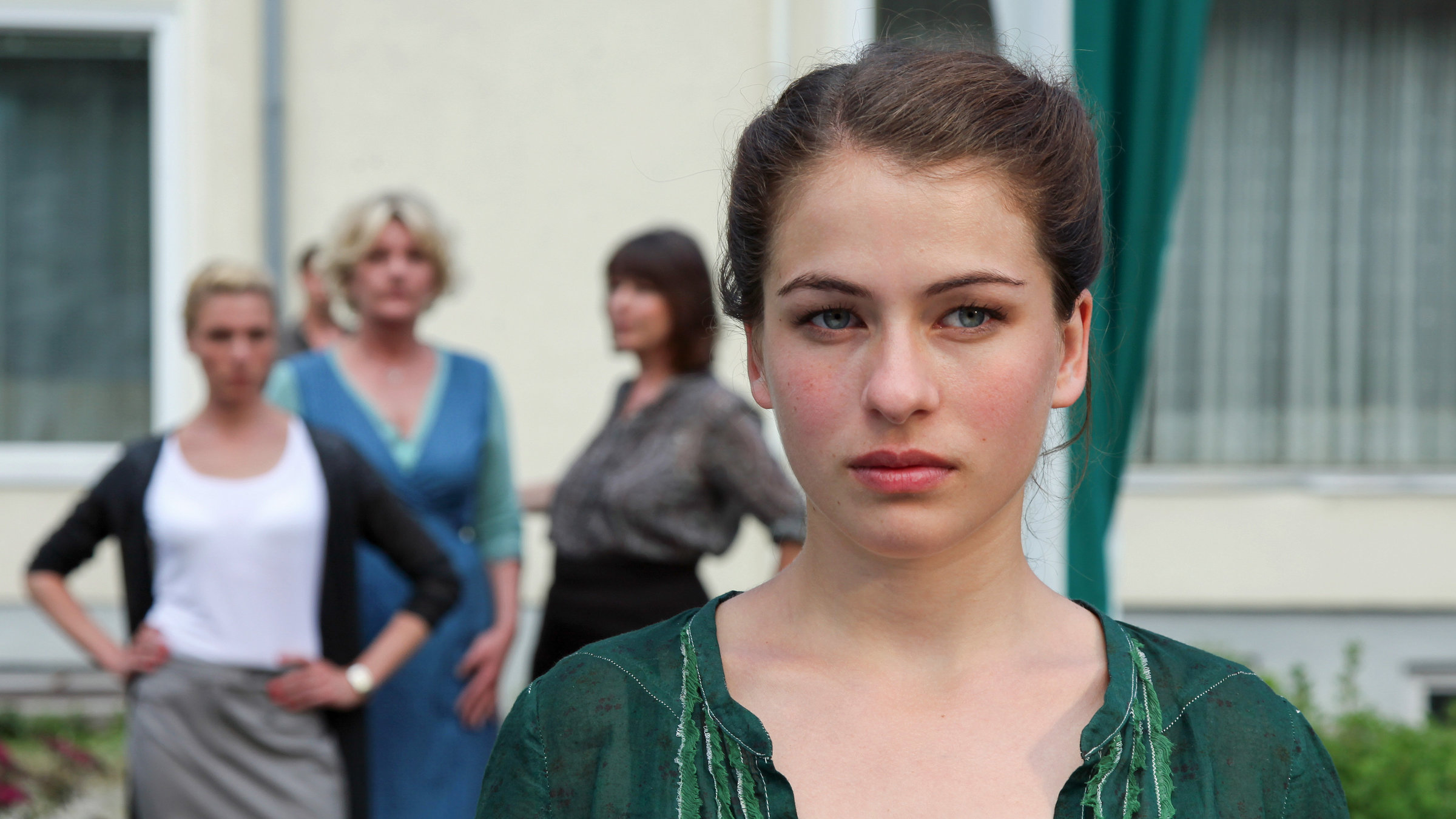 "Die Fremde und das Dorf": Henriette Confurius (Rosaria) schaut erst aus dem Bild. Hinter ihr stehen (unscharf zu sehen) drei Frauen und schauen zu ihr.