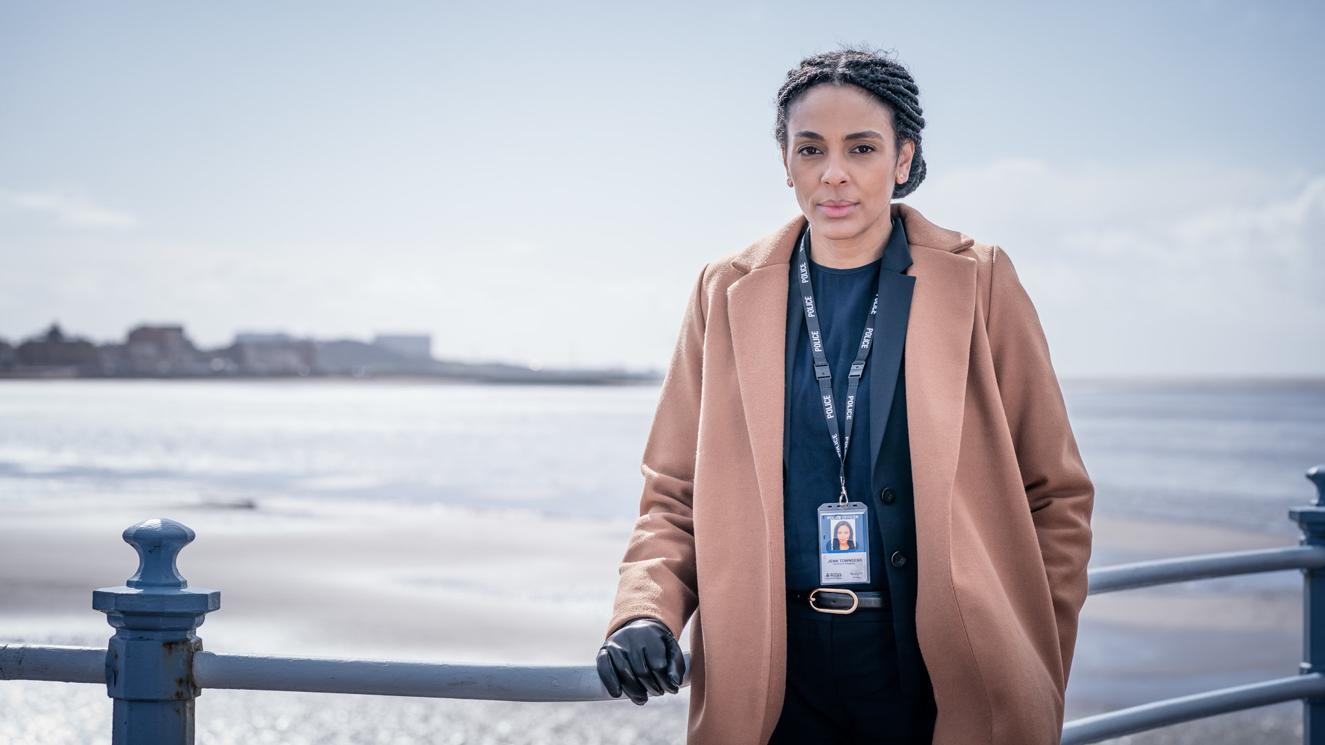 "The Bay - Neustart": DS Jenn Townsend (Marsha Thomason) lehnt sich an ein Geländer und schaut dabei konzentriert in die Kamera. Im Hintergrund ist das raue Meer zu erkennen, während am Horizont die Umrisse von einigen Gebäuden zu sehen sind.