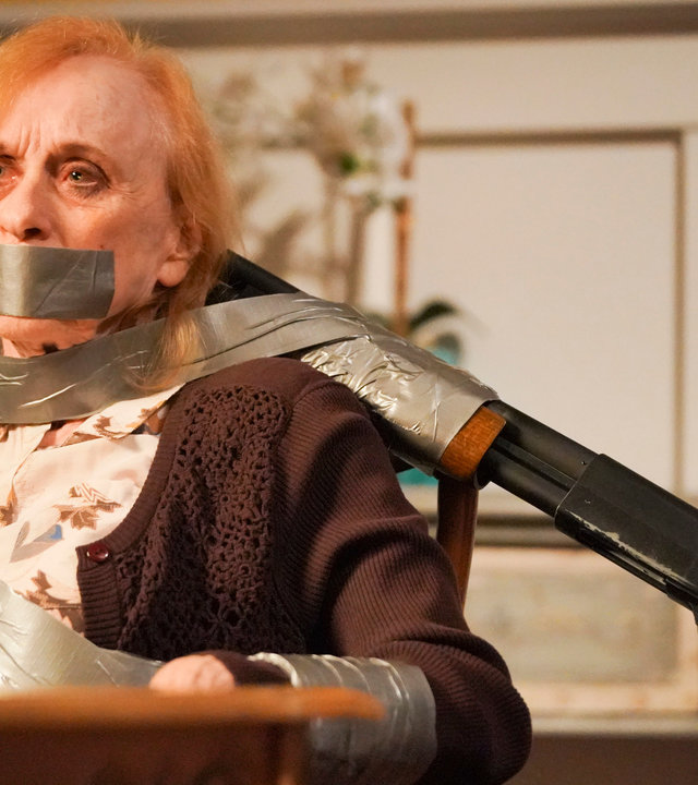 "The Rookie - Menschenjagd": Sallie (Jeannie Epper) ist mit Paketband an einen Stuhl gefesselt. Sie hat einen ängstlichen Gesichtsausdruck. Ein Gewehr ist mit Tape an der Stuhllehne befestigt und auf Sallies Kopf gerichtet.