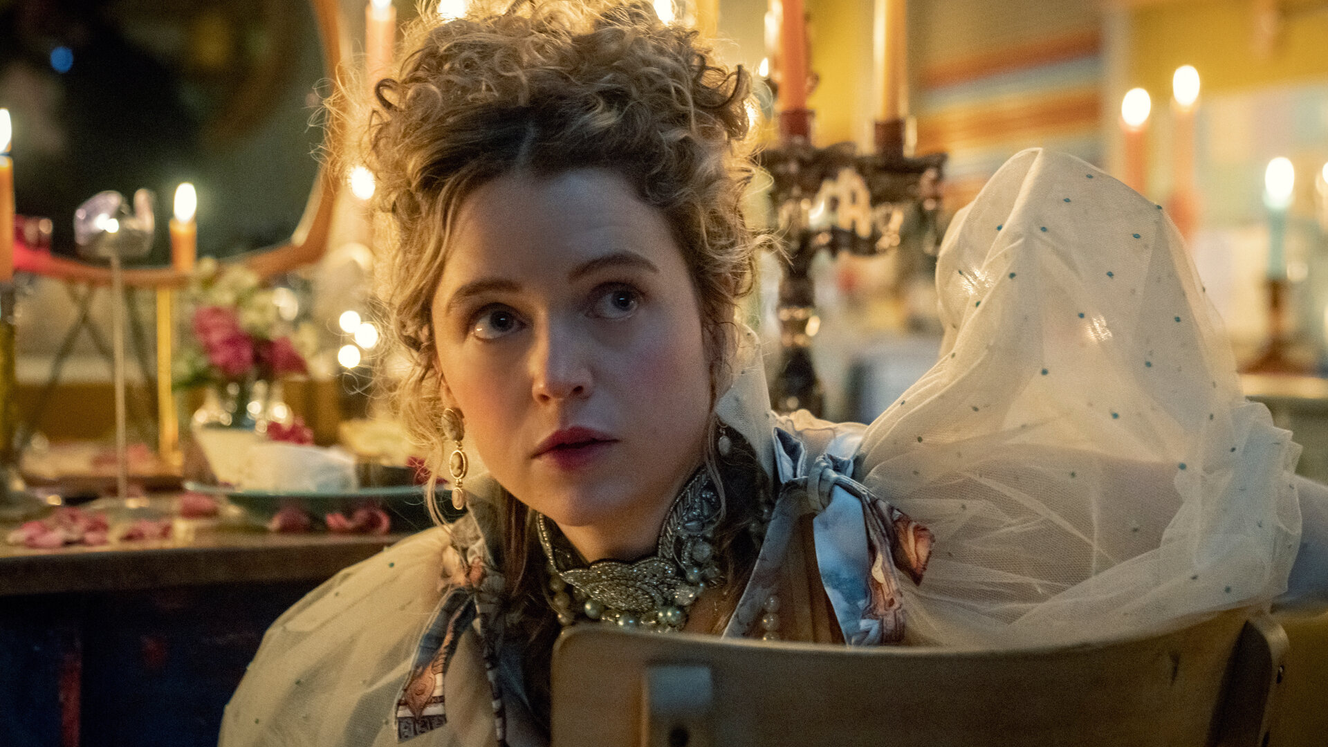 "Extraordinary - Der muntere Monarch": Carrie (Sofia Oxenham) sitzt auf dem Stuhl vor dem Spiegel, ist wie für eine Adelige üblich, stark geschminkt und trägt ein aufwendiges Kleid mit Puffärmeln.