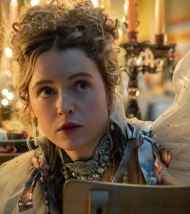 "Extraordinary - Der muntere Monarch": Carrie (Sofia Oxenham) sitzt auf dem Stuhl vor dem Spiegel, ist wie für eine Adelige üblich, stark geschminkt und trägt ein aufwendiges Kleid mit Puffärmeln.