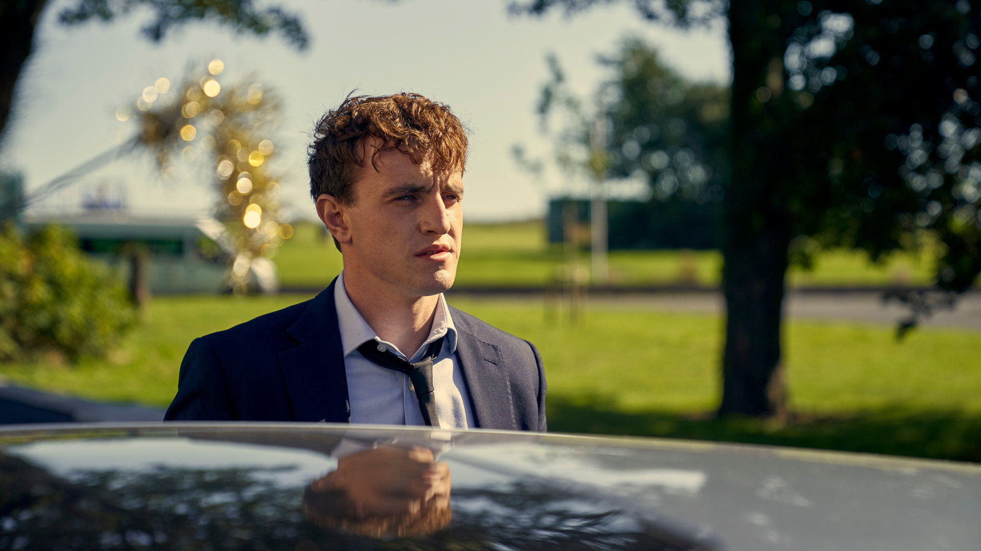 "Normal People - Depression": Connell (Paul Mescal) steht im Anzug neben einem schwarzen Auto und schaut traurig in die Ferne.