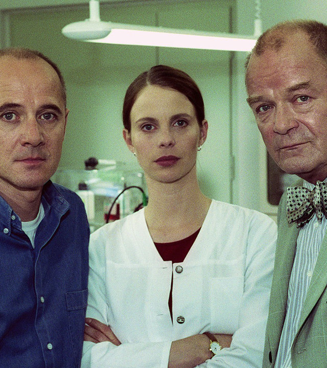 "Der letzte Zeuge - Der Tag, an dem ein Vogel vom Himmel fiel": Dr. Kolmaar (Ulrich Mühe), Prof. Bondzio (Dieter Mann) und Dr. Leilah Berg (Julia Jäger) stehen im Labor und blicken in die Kamera.