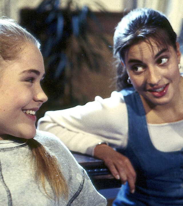 "Alle meine Töchter - Karrieresprünge": Patricia Sanwaldt (Floriane Eichhorn) und Sylvie von Wettenberg (Julia Dahmen) sitzen im Wohnzimmer nebeneinander und lächeln sich bedeutungsvoll an.