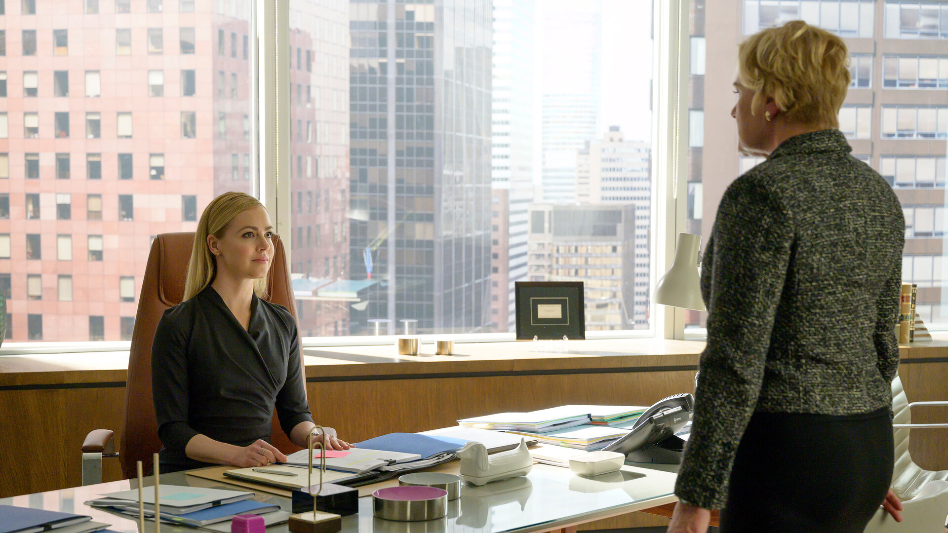 "Suits - Zwangsverwaltung": Katrina (Amanda Schull) sitzt am Schreibtisch, auf dem etliche Akten und Dokumente ausgebreitet liegen. Vor ihr steht Faye (Denise Crosby), die ihre Hände auf zwei Stühle neben ihr gelegt hat.