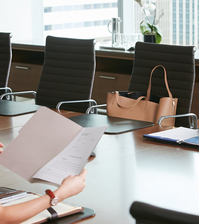"Suits - Stunde der Wahrheit": Rachel (Meghan Markle) und Claire (Troian Bellisario) sitzen sich am Tisch eines Konferenzraums gegenüber. Rachel hat ihre gefalteten Hände auf Dokumente auf dem Tisch gelegt und schaut zu Claire, die in Unterlagen blättert.