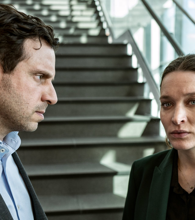 "Hidden Agenda II - Verrat (6)": Daniel (Joel Spira) und Emily (Josefin Asplund) stehen vor einer Treppe im Gerichtsgebäude. Sie wirkt verunsichert, er blickt in ihre Richtung.