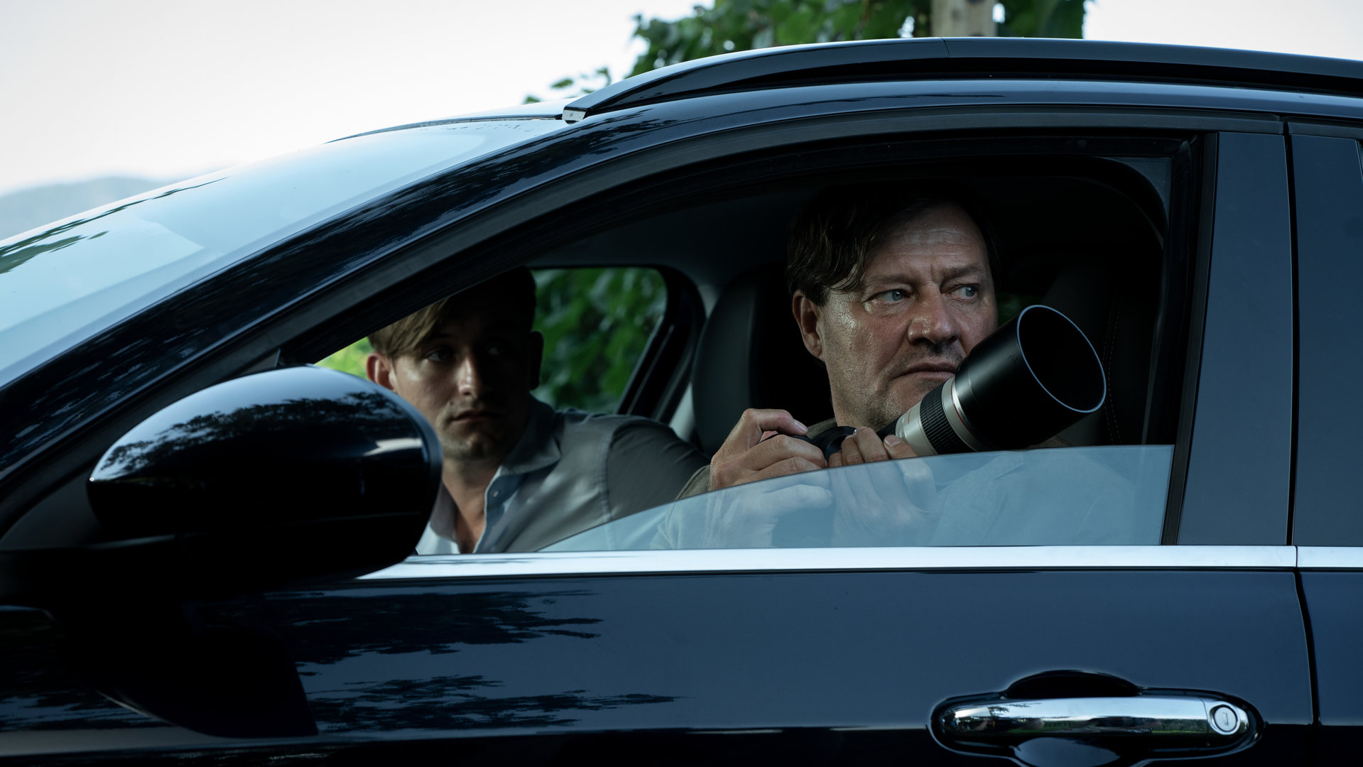 "Im Netz der Camorra": Silvio Bernatti (Lukas Watzl) und Adrin Erlacher (Harald Windisch) sitzen in einem Auto und schauen aus dem Fenster der Fahrerseite in die gleiche Richtung. Erlacher hat eine Kamera mit Zoomobjektiv in der Hand.