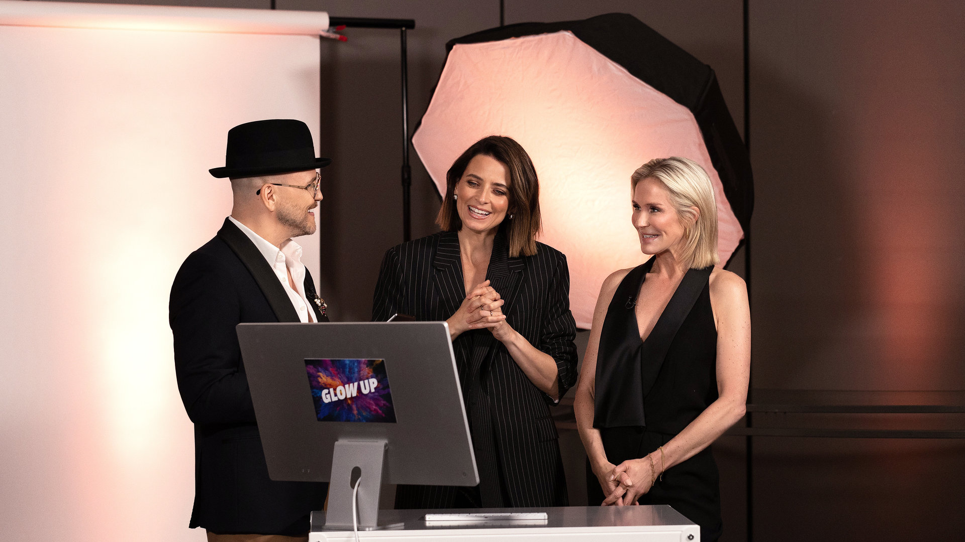 "Glow Up - Deutschlands nächster Make-up-Star: Red Carpet": Juror Armin Morbach, Gastjurorin und Top-Model Eva Padberg und Jurorin Loni Baur betrachten die Looks der MUAs auf einem Bildschirm. Die drei sind im Gespräch und schauen nicht in die Kamera. Im Hintergrund eine Fotografenlampe.
