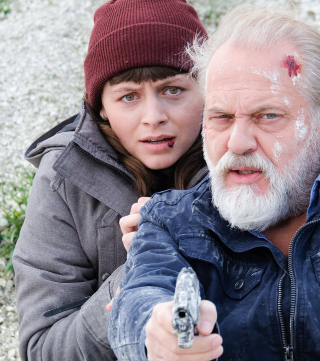 "Der Alte - Tod am Kliff": Paula Voss (Antonia Breidenbach) versteckt sich hinter der Schulter ihres Vaters Richard Voss (Jan-Gregor Kremp), der mit einer Schürfwunde am Kopf und mit gezogener Pistole in der Hand an einen Abhang mit Schutt gelehnt sitzt.