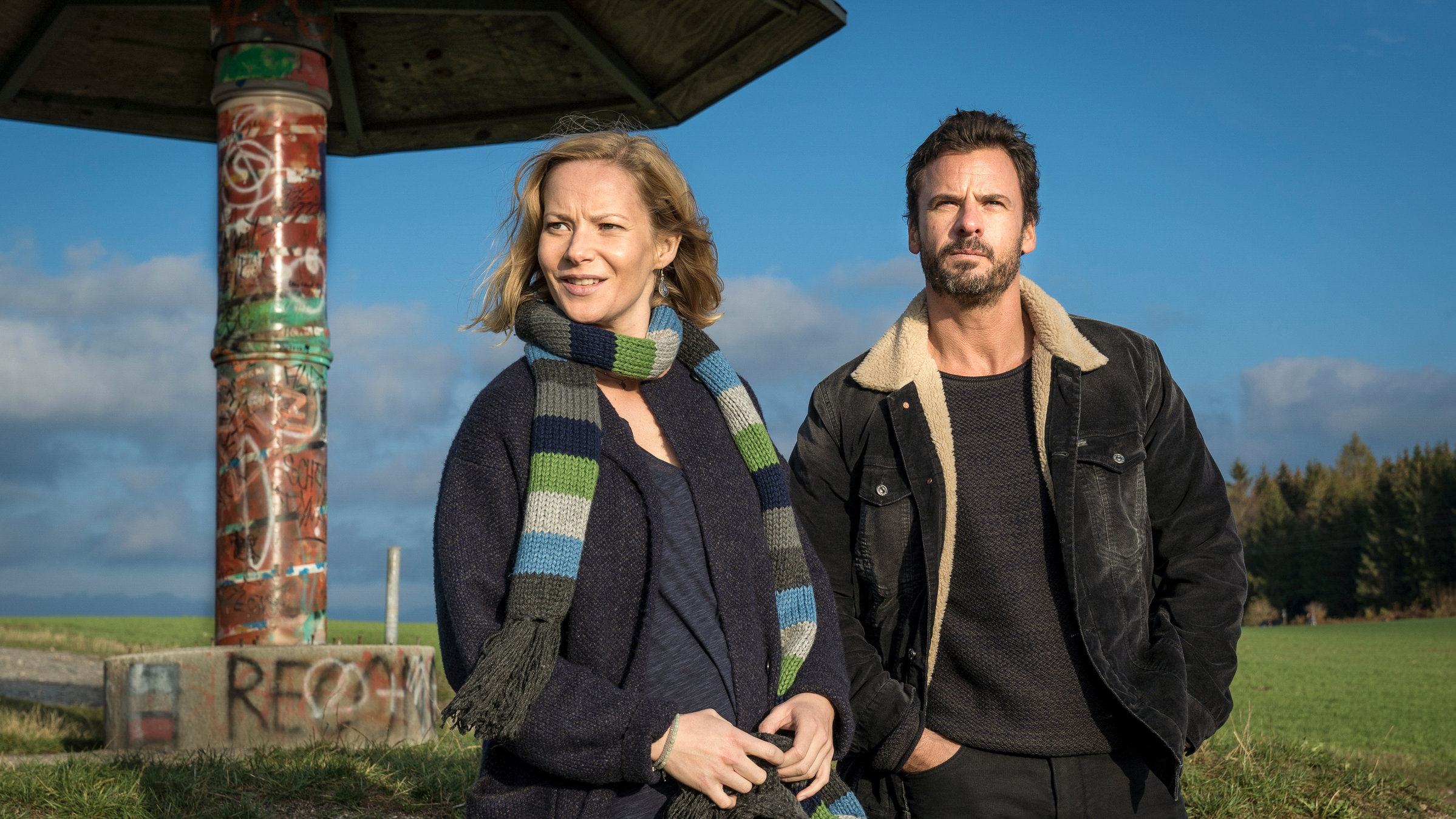 "Erzgebirgskrimi - Der Tote im Stollen": Försterin Saskia Bergelt (Teresa Weißbach) und Kommissar Ralf Adam (Stephan Luca) stehen nebeneinander vor einem pilzförmigen Unterstand. Saskia schaut zur Seite, während Ralf in die Ferne sieht.