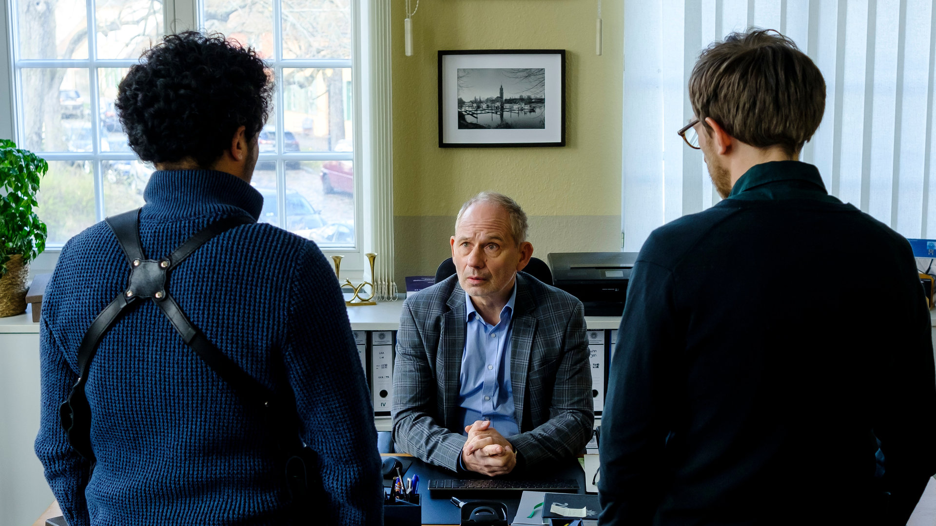 "SOKO Potsdam - Bittersüßer Tod": David Grünbaum (Omar El-Saeidi) und Christoph Westerman (Hendrik von Bültzingslöwen) stehen mit dem Rücken zur Kamera vor dem Schreibtisch ihres Chefs Bernhard Henschel (Michael Lott). Dieser schaut zu David.