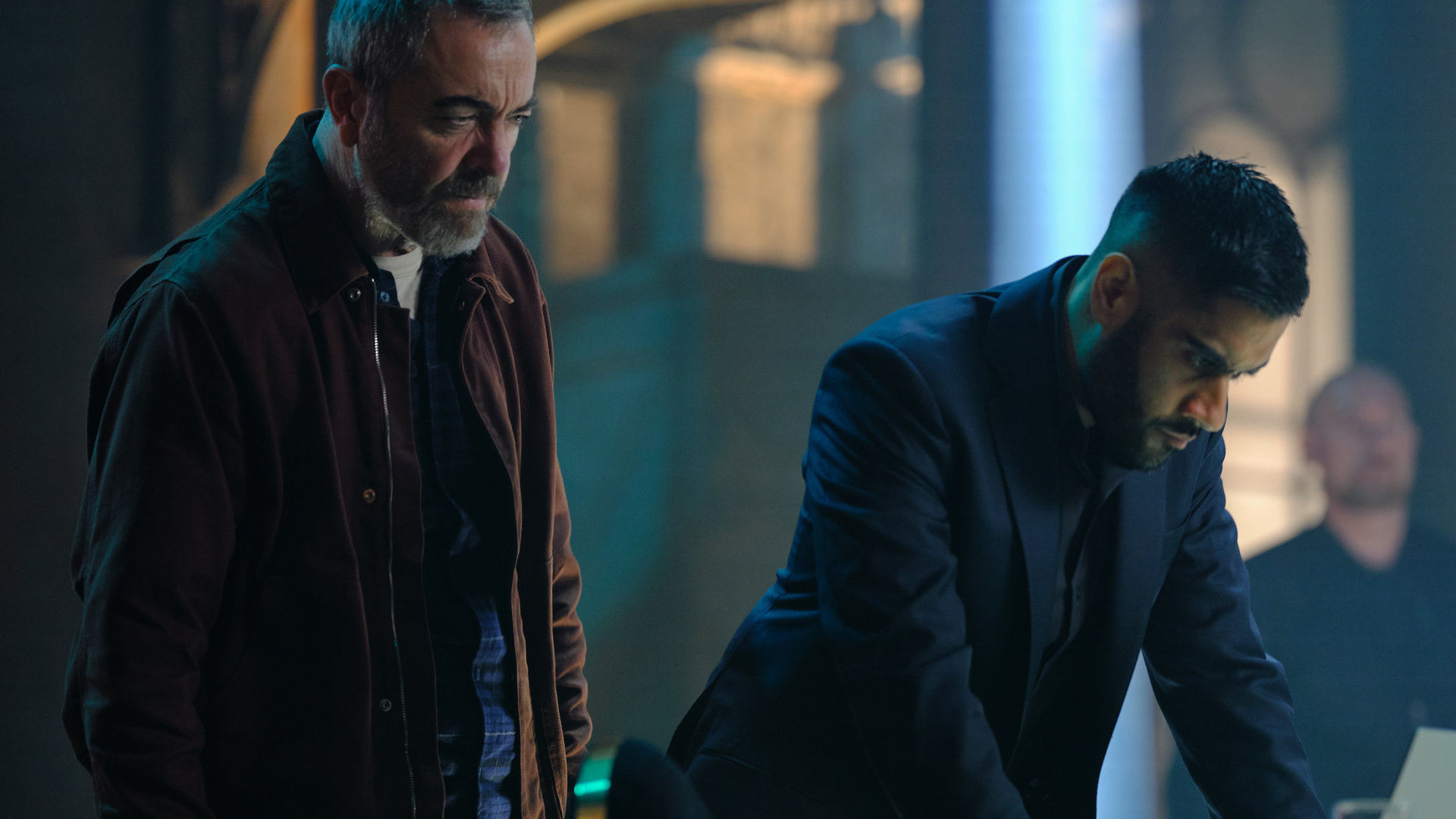 "Suspect - Folge 4: Jaisal": Jaisal (Sacha Dhawan) und Danny (James Nesbitt) stehen nebeneinander vor einem Schreibtisch und schauen sich die darauf liegenden Akten an.