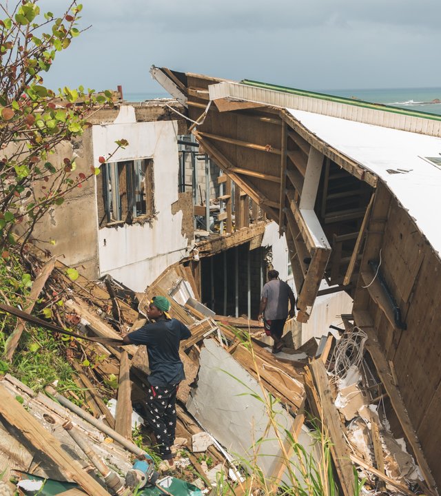 "planet e.: Karibische Sturmfront - Wie der Inselstaat Dominica dem Klimawandel trotzt": Mann in den Trümmern eines Hauses nach dem Hurrikan an einer Küste.