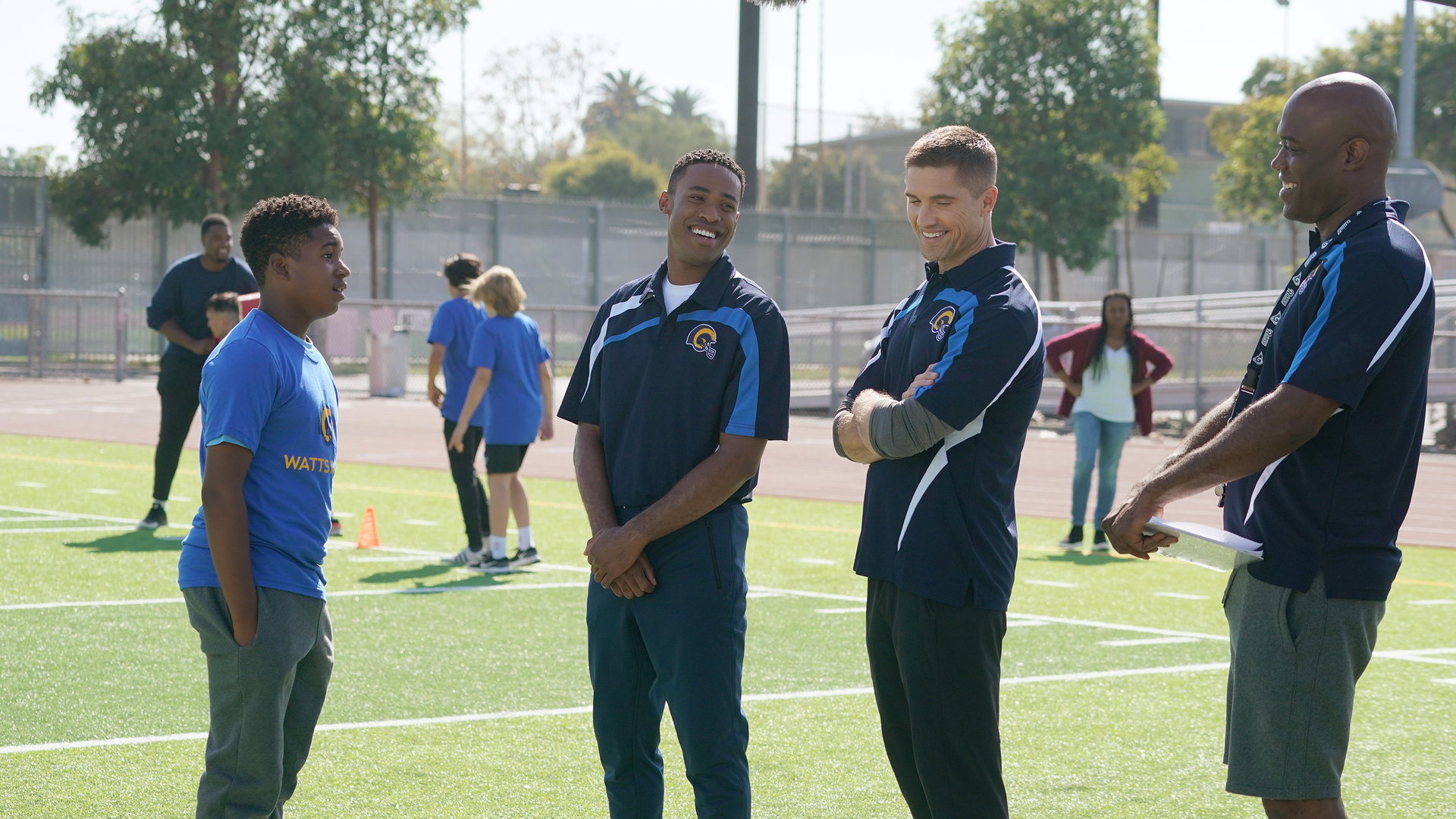 "The Rookie - Sicher ist sicher": Tim Bradford (Eric Winter) und Jackson West (Titus Making Jr.) stehen, sich amüsierend, zwischen dem Trainer und einem Jungen aus der Mannschaft.