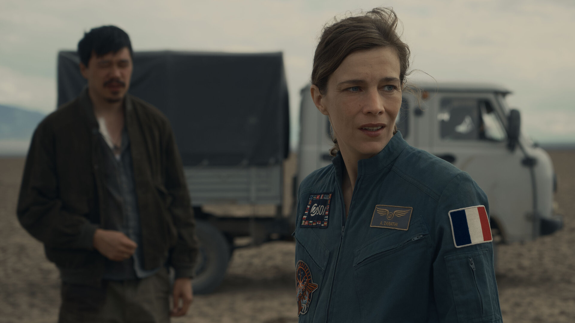 "Infiniti - Schwarze Sonne": Isaak (Daniyar Alshinov) und Anna (Céline Sallette) stehen gemeinsam vor einem Lastwagen in der kasachischen Steppe und schauen sich nachdenklich um.