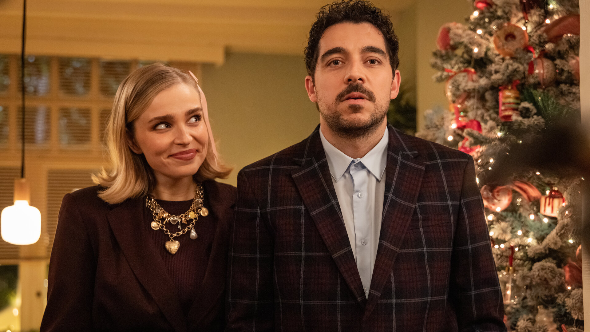 "Single Bells - Only Losers for Annie? - Izzy": Mina (Julie Van den Steen) und Roel (Robbert Vervloet) stehen in ihrem Wohnzimmer. Mina lächelt. Im Hintergrund steht ein üppig dekorierter Weihnachtsbaum.