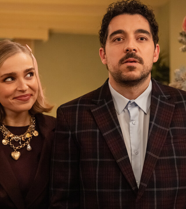 "Single Bells - Only Losers for Annie? - Izzy": Mina (Julie Van den Steen) und Roel (Robbert Vervloet) stehen in ihrem Wohnzimmer. Mina lächelt. Im Hintergrund steht ein üppig dekorierter Weihnachtsbaum.