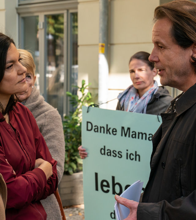 "Letzte Spur Berlin - Taufpatin": Jessica Papst (Paula Kalenberg) und Mina Amiri (Jasmin Tabatabai) stehen nebeneinander vor Martin Lipp (Christian Kuchenbuch). Um sie herum stehen mehrere Frauen mit Plakaten.