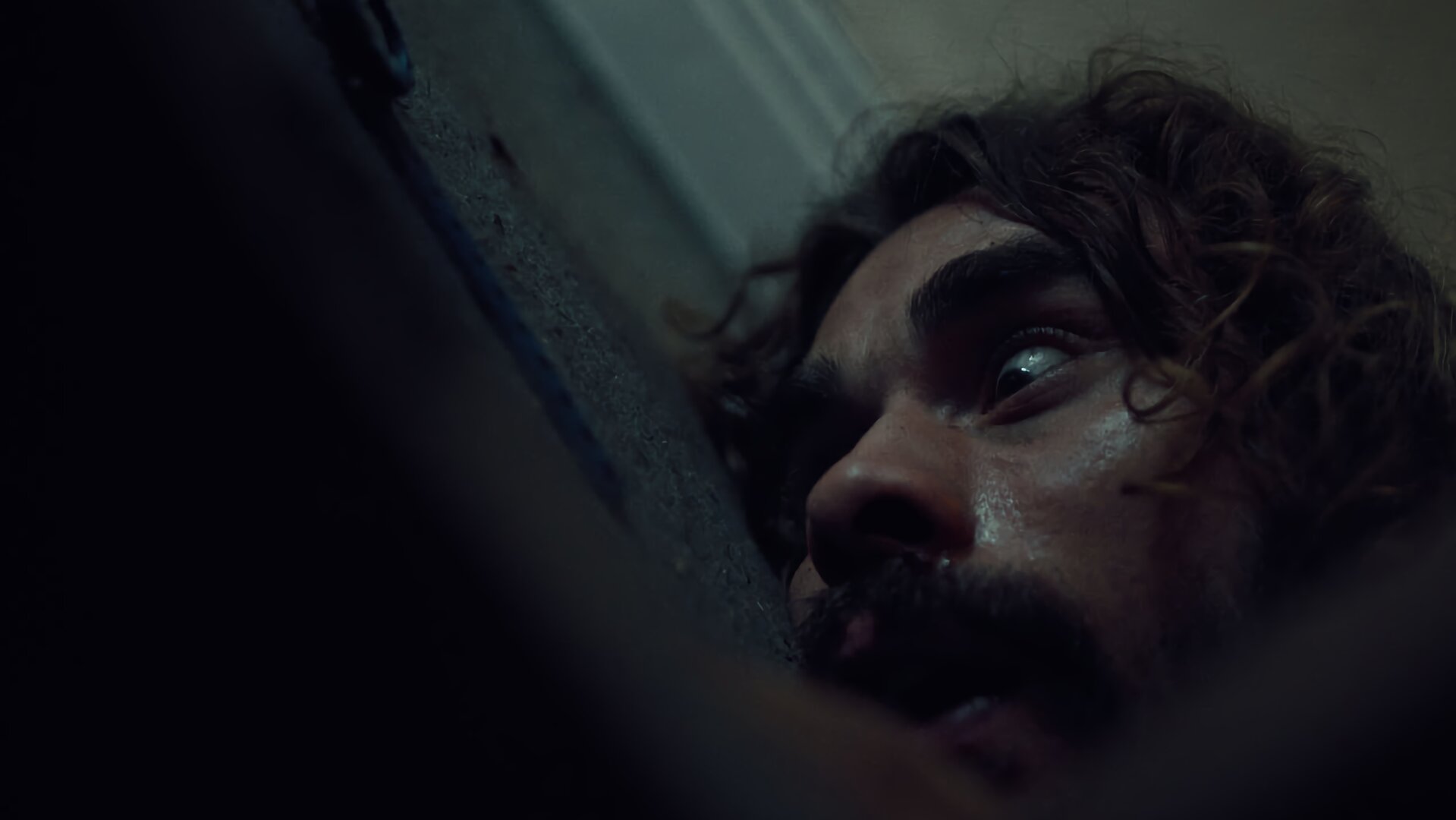 "Moresnet - The Book of Death: Rien ne va plus": Nahaufnahme: Ben Schotz (Boris Van Severen) liegt mit angst- und schmerzerfülltem Blick auf dem Teppichboden eines Zimmers.