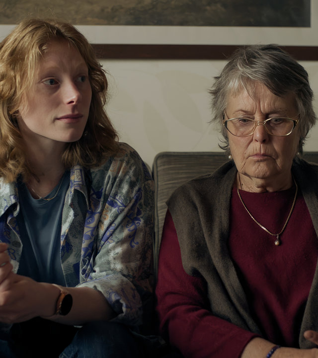 "SOKO Stuttgart - Enkeltrick": Fiona Kimmerle (Dana Herfurth) und Irmgard Löffler (Petra Kelling) sitzen auf einem alten grauen Sofa. Fiona blickt sorgenvoll zur Seite, Irmgard hat den Blick gedankenverloren gesenkt.