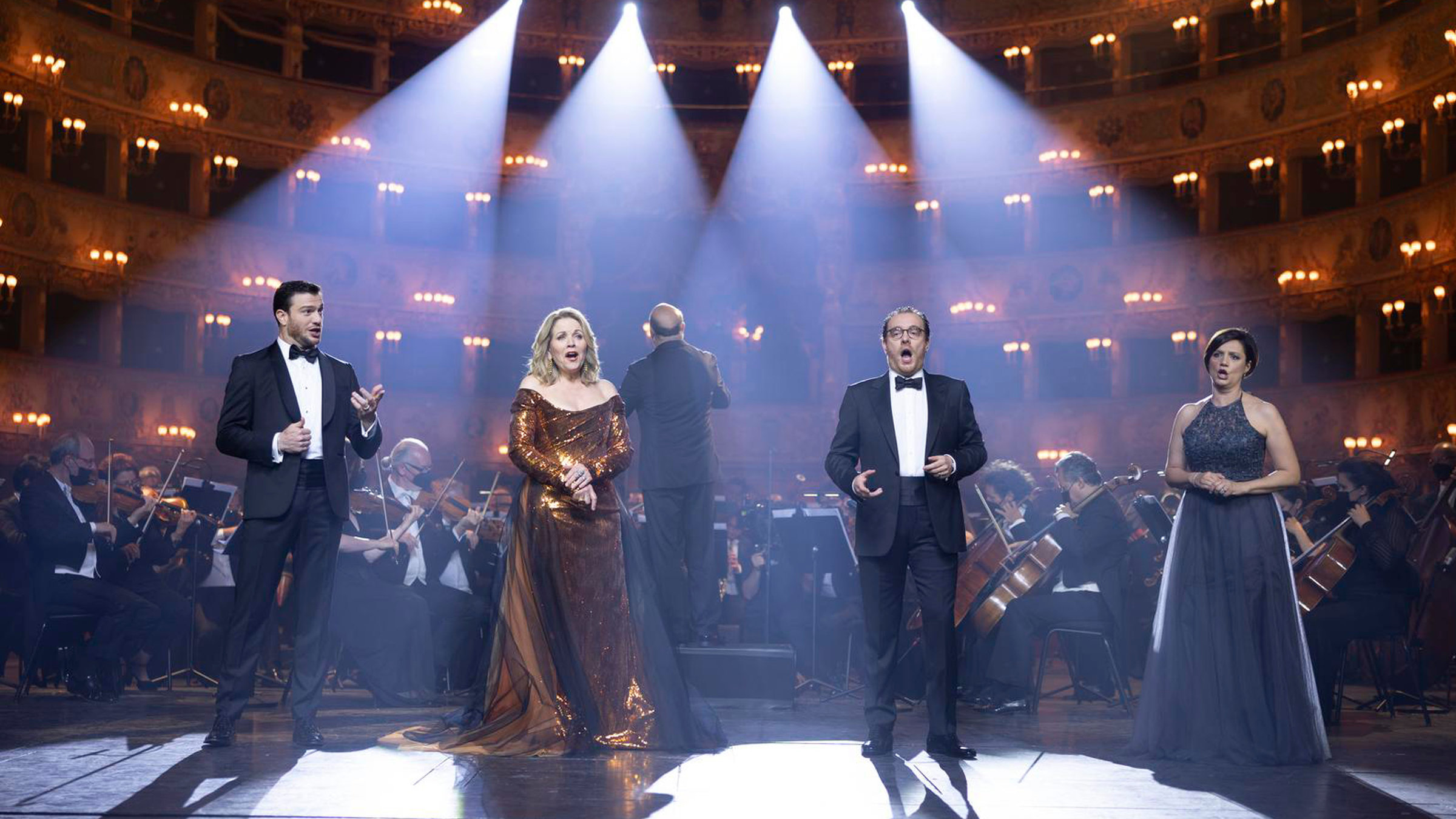 "Musikstadt Venedig": v. links nach rechts auf der Bühne stehen Mattia Olivieri (Bariton), Renée Fleming (Sopran), Francesco Meli (Tenor) und Paola Gardina ( Mezzosopran). Im Hintergrund das Orchester und die beleuchteten Ränge des Theaters.