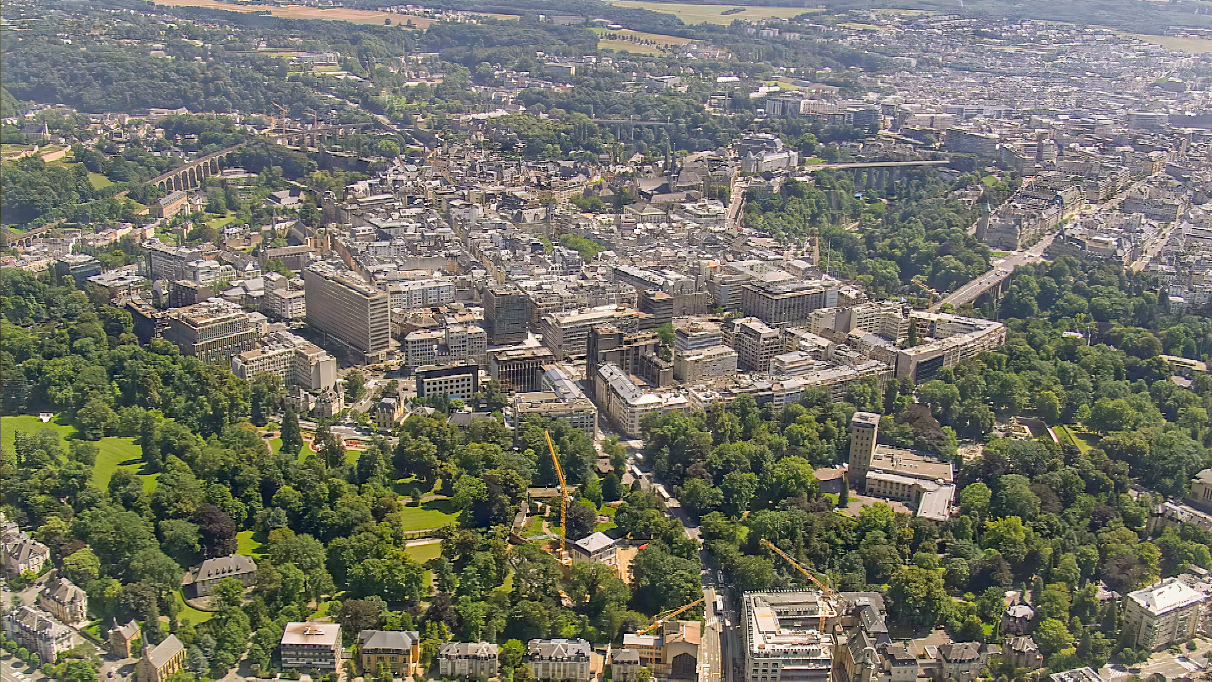 "Im Flug über Luxemburg und Belgien": Luftaufnahme einer Stadt durchzogen von Grünflächen und Bäumen.