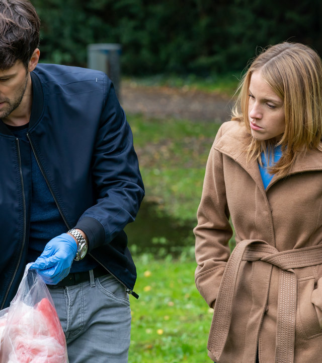 "Letzte Spur Berlin - Herzdame": Alex von Tal (Aleksandar Radenkovic) und Jessica Papst (Paula Kalenberg) stehen in einem Park nebeneinander. Alex trägt blaue Gummihandschuhe. Mit der linken Hand hält er einen durchsichtigen Plastikbeutel in den er mit der rechten Hand einen blutigen Brautschleier stopft. Beide blicken auf den Schleier.