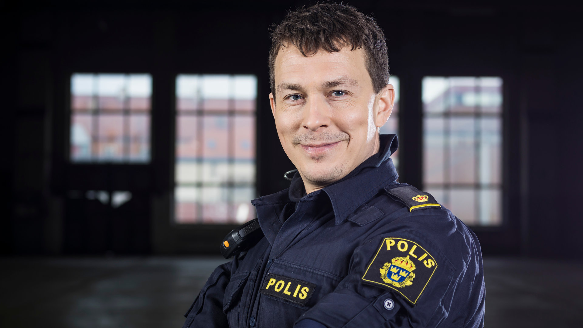 "Thin Blue Line - Aufruhr": Magnus (Oscar Töringe) steht mit verschränkten Armen in einem dunklen Raum und blickt grinsend in Richtung Kamera.