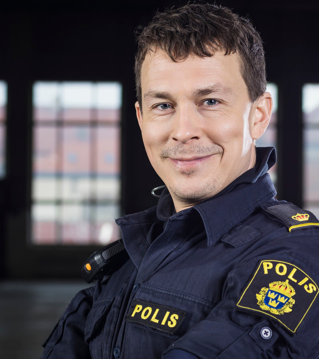 "Thin Blue Line - Aufruhr": Magnus (Oscar Töringe) steht mit verschränkten Armen in einem dunklen Raum und blickt grinsend in Richtung Kamera.