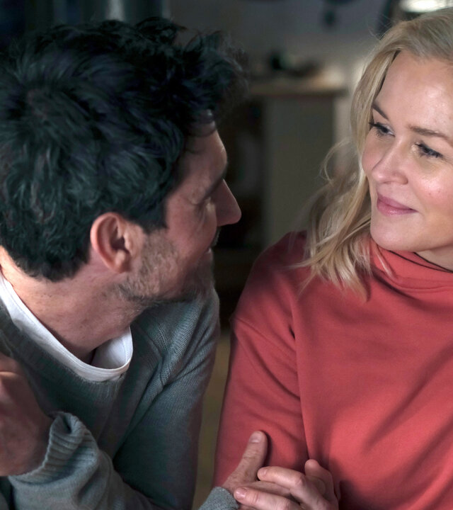 "Lena Lorenz - Benita und Muck": Nahaufnahme: Lena Lorenz (Judith Hoersch) und Rob Manzini (Seán McDonagh) sitzen dicht nebeneinander, halten sich an den Händen und lächeln sich zärtlich an.