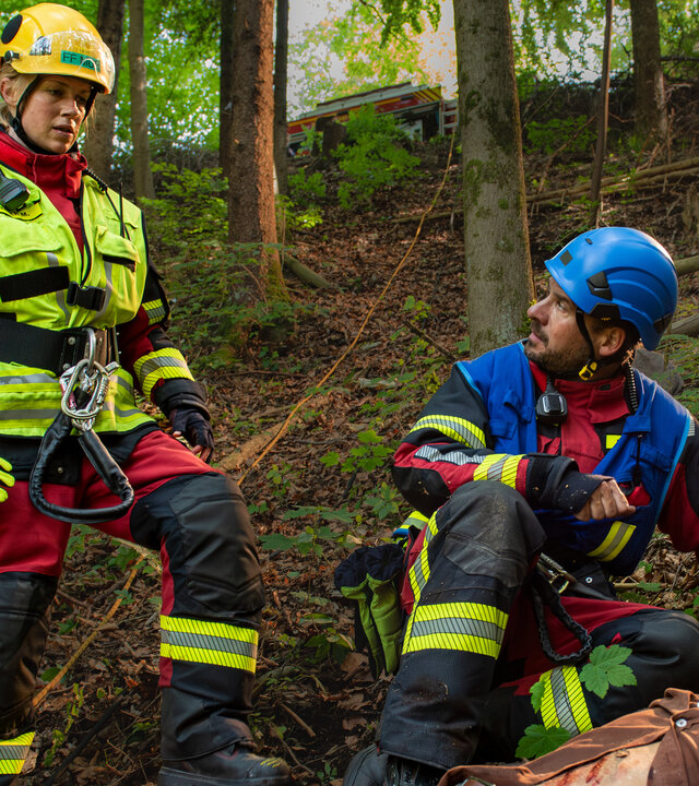 "Marie fängt Feuer - Neuanfänge": Paul (Eisi Gulp) liegt verletzt im Wald auf dem Boden. Peter (Stephan Luca) kniet neben dem Verletzten und kümmert sich um diesen. Marie (Christine Eixenberger) steht durch ein Seil abgesichert etwas neben den beiden.