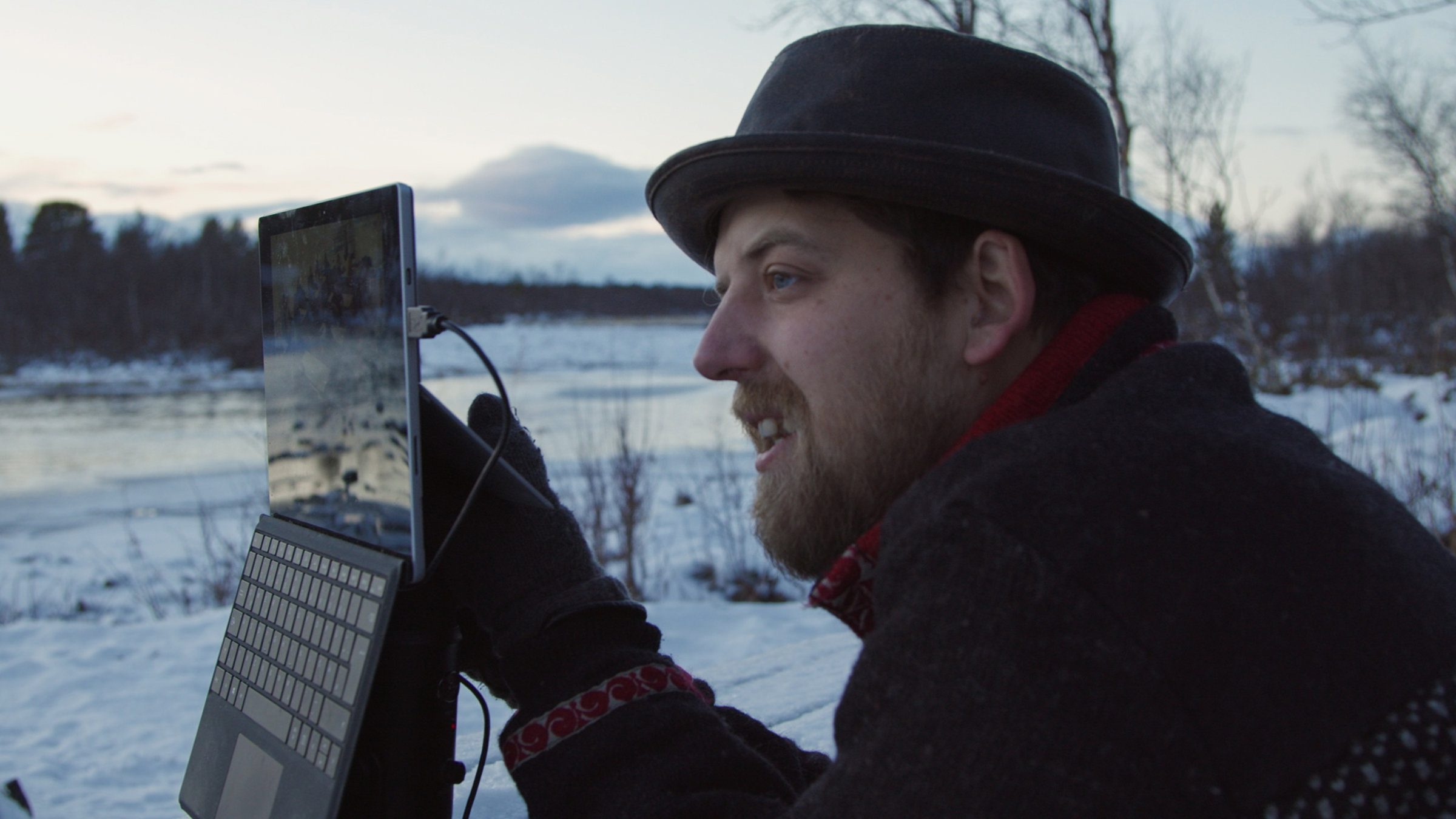 "Jonny Island": Ein lächelnder Mann mit Hut und Bart hält einen Laptop in die Höhe. Im Hintergrund eine winterliche Landschaft.