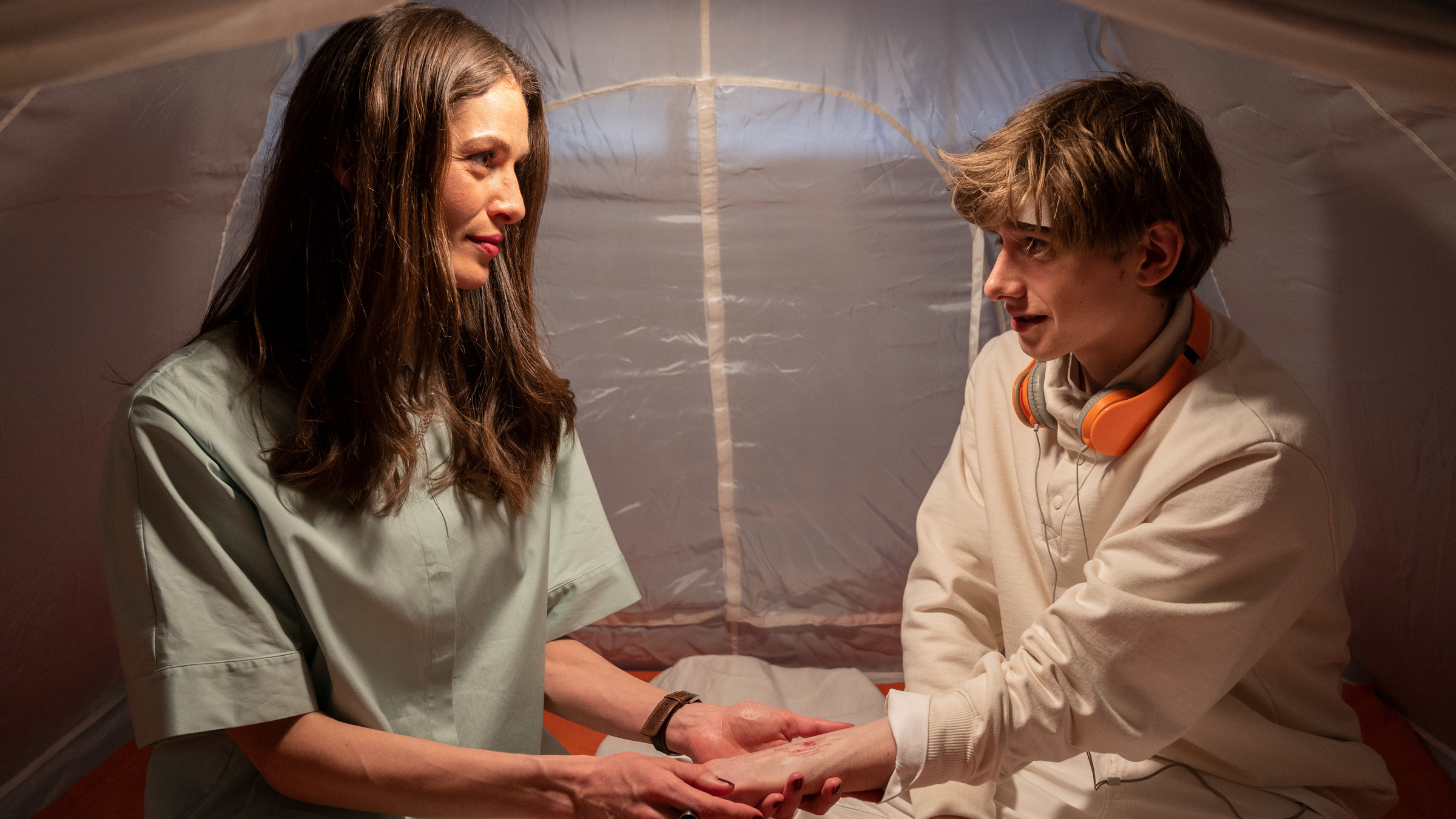 "SOKO Stuttgart – Bling Bling": Rebecca (Anna Puck) und Vincent Fiori (Johannes Geller) sitzen in einem weißen Zelt. Rebecca hält fürsorglich Vincents Hand, an der eine Verletzung zu sehen ist. Die beiden lächeln sich liebevoll an.