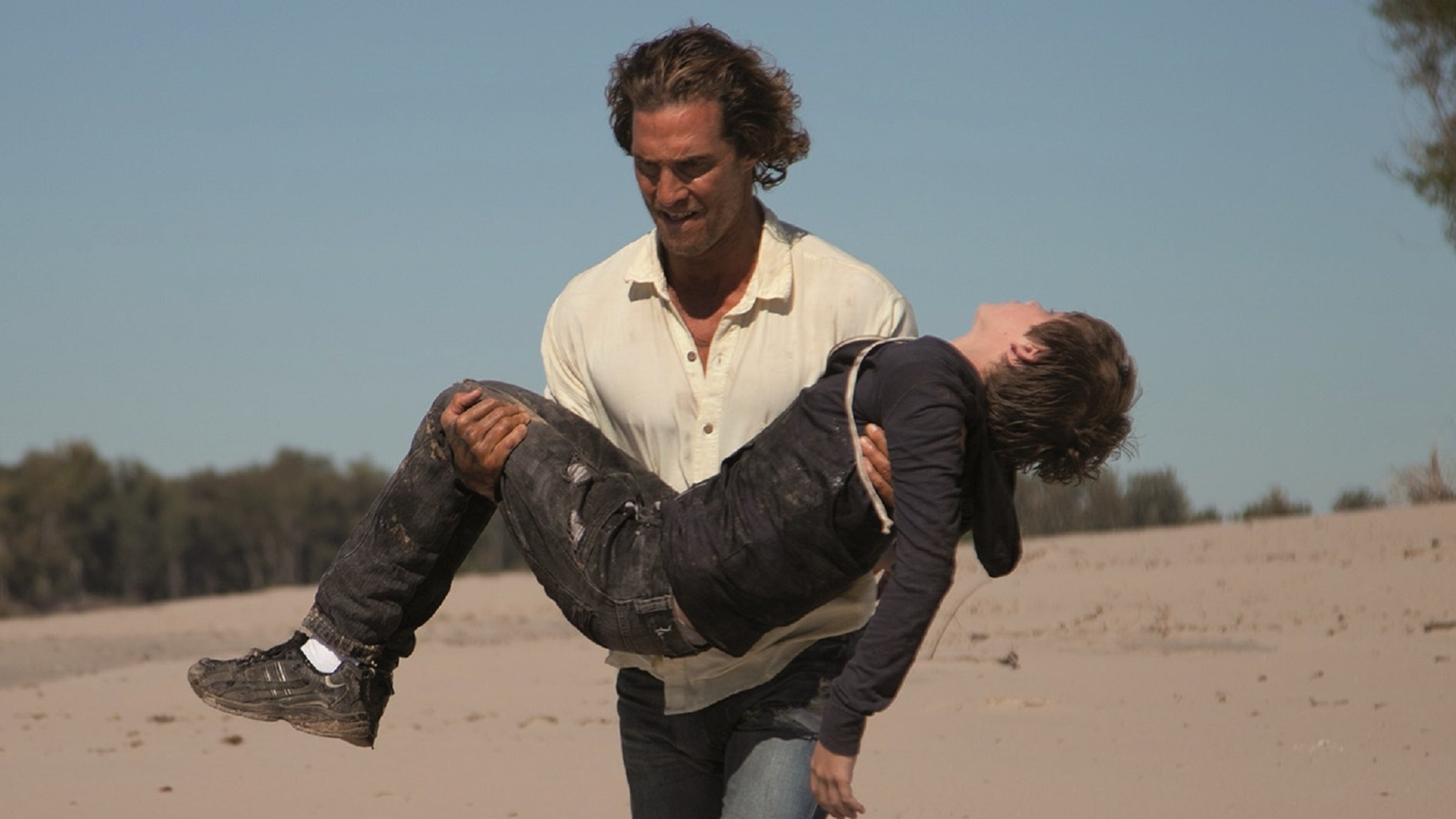 "Mud - Kein Ausweg": Mud (Matthew McConaughey) läuft in einer zerrissenen Jeans über einen Sandstrand und trägt dabei Ellis (Tye Sheridan) in seinen Armen, der offensichtlich das Bewusstsein verloren hat.