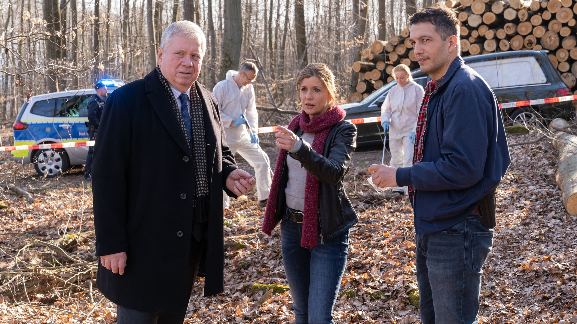 "Der Staatsanwalt - Die letzte Absage": Oberstaatsanwalt Bernd Reuther (Rainer Hunold), Hauptkommissarin Kerstin Klar (Fiona Coors) und Oberkommissar Max Fischer (Max Hemmersdorfer) stehen auf einer Lichtung im Wald. Im Hintergrund sind Spurensicherer in weißen Overalls bei der Arbeit zu sehen. Ein Polizeiauto und ein Bestattungswagen stehen am Waldrand.