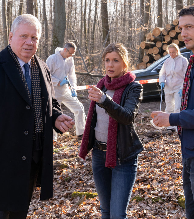 "Der Staatsanwalt - Die letzte Absage": Oberstaatsanwalt Bernd Reuther (Rainer Hunold), Hauptkommissarin Kerstin Klar (Fiona Coors) und Oberkommissar Max Fischer (Max Hemmersdorfer) stehen auf einer Lichtung im Wald. Im Hintergrund sind Spurensicherer in weißen Overalls bei der Arbeit zu sehen. Ein Polizeiauto und ein Bestattungswagen stehen am Waldrand.