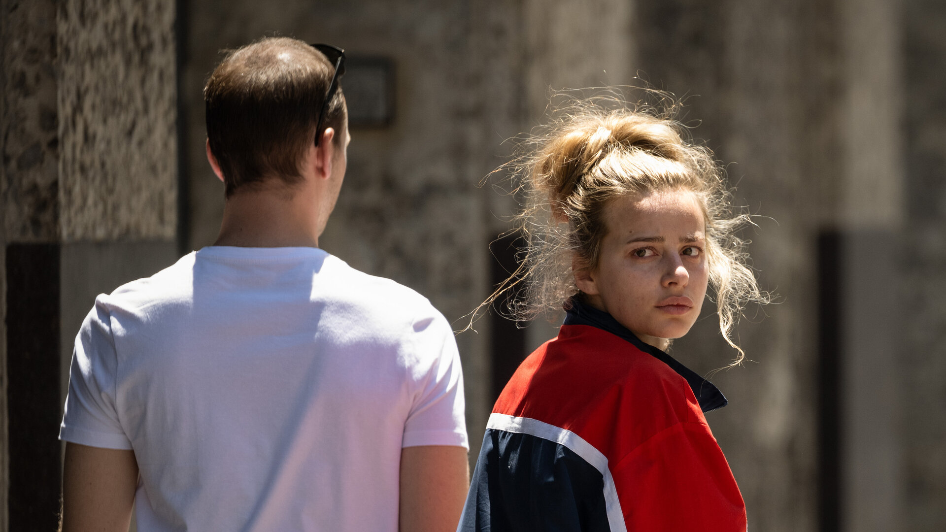 "Kidnapped: The Chloe Ayling Story – Die Ermittlung": Chloe (Nadia Parkes) und MD (Julian Świeżewski) gehen nebeneinander an einem großen Gebäude entlang. Sie schaut sich nach hinten um.